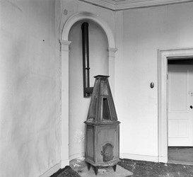 <p>Foto uit 1982 van de kamer van de jonkheer met in de hoek een kachelnis met kolomkachel. Hoewel dit soort schouwen meestal uit het begin van de 19e eeuw dateren is de gehele indeling van deze ruimte pas kort voor 1900 tot stand gekomen.</p>
